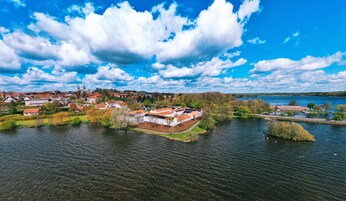 Vista aérea de un pueblo a orillas de un lago, con edificios históricos, una iglesia destacada y un puente que lo conecta.