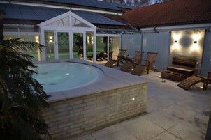 Una piscina con borde de piedra, rodeada de sillones de descanso y un patio cubierto con muro de ladrillo y banco de madera.