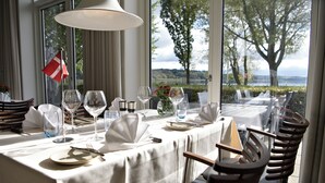 A dining table set for four with a flag, wine glasses, and a view of the outdoors. - Golf Hotel Viborg (Viborg)