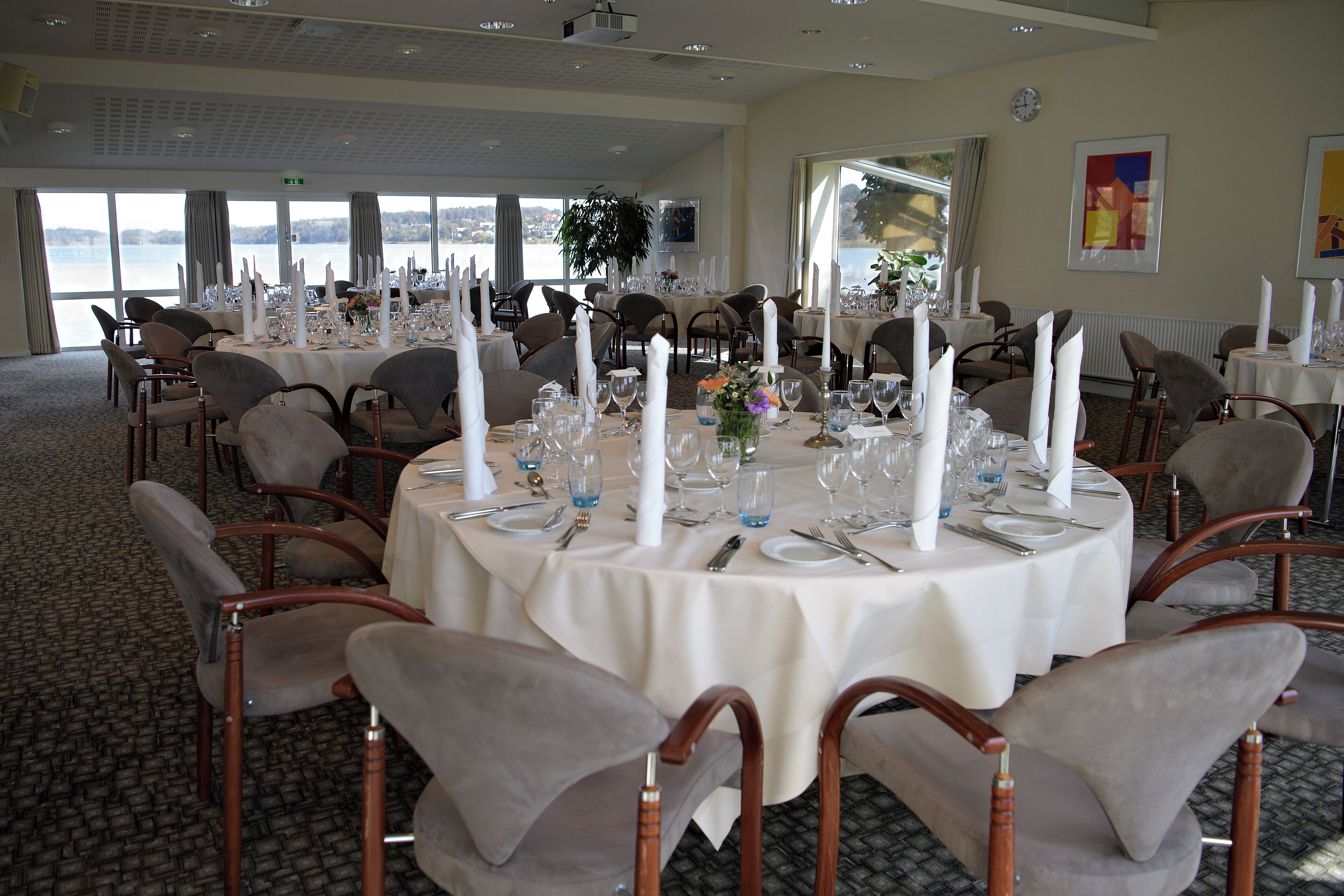 Un espace repas avec des tables rondes dressées pour un repas formel, entouré de chaises rembourrées.
