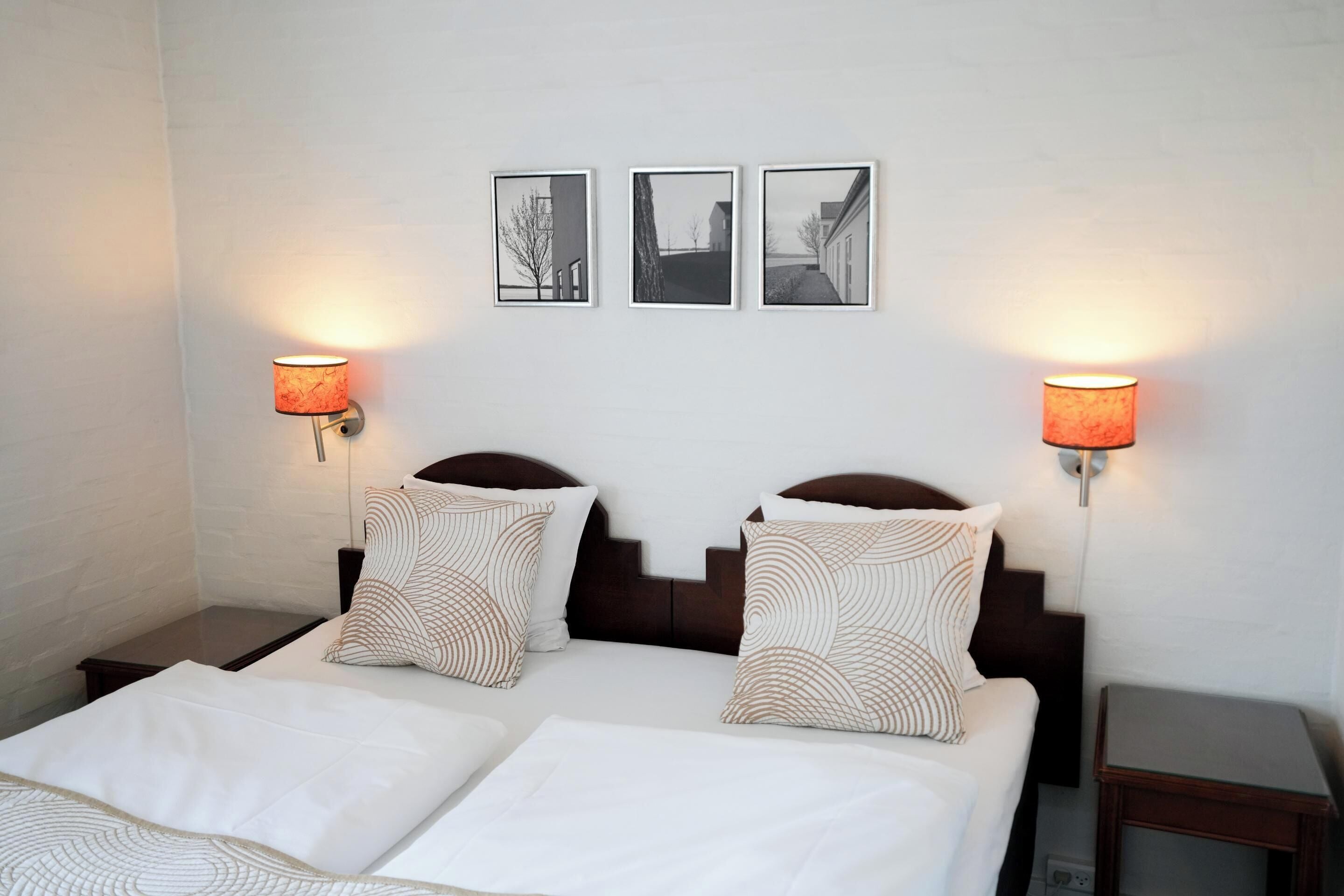 A hotel room with a double bed, two nightstands, and three framed pictures on the wall.