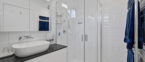 A modern bathroom with a white sink, black countertop, and a glass-enclosed shower.