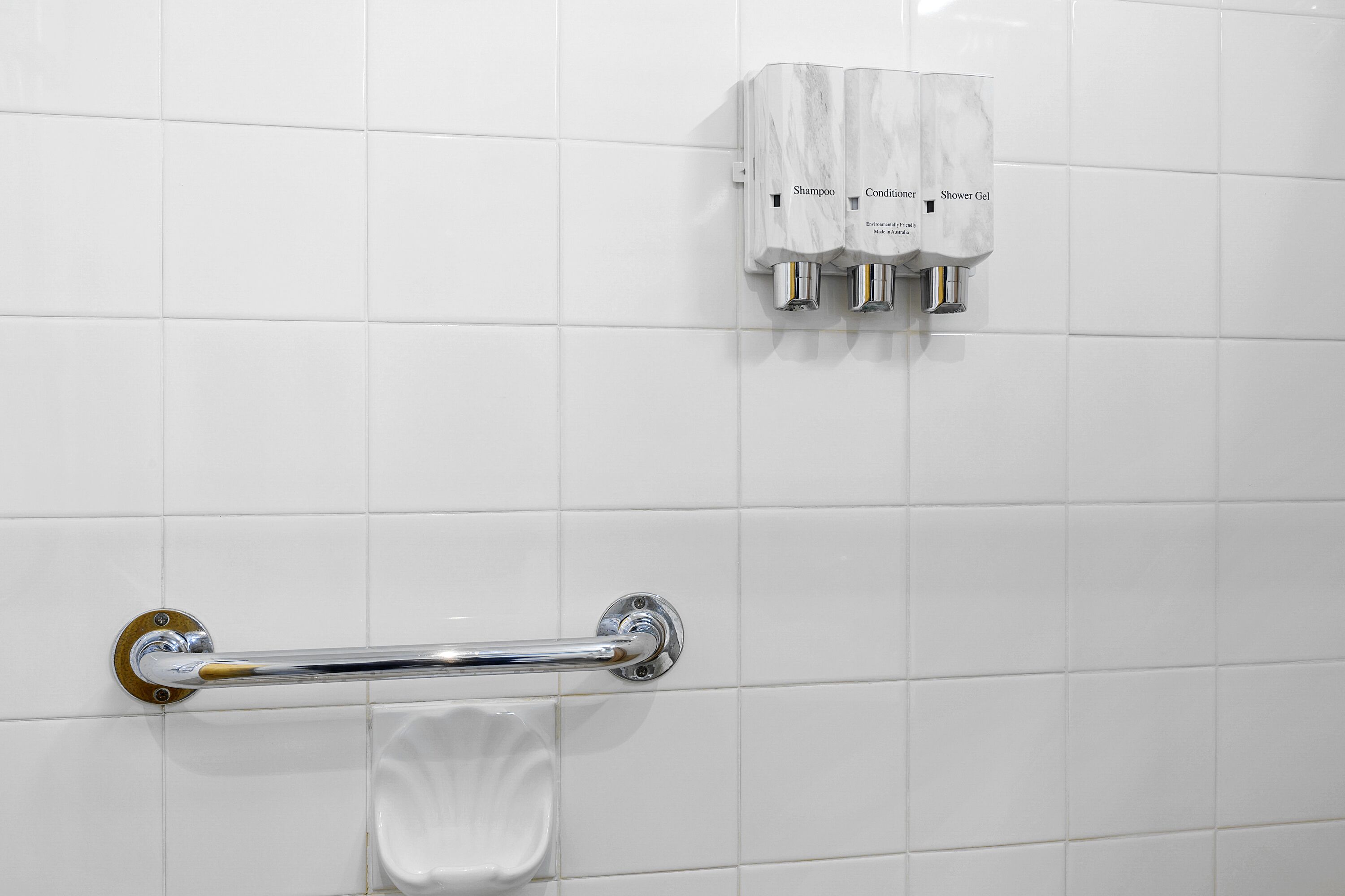 A bathroom with white tiles, a hand dryer, and a towel rack.