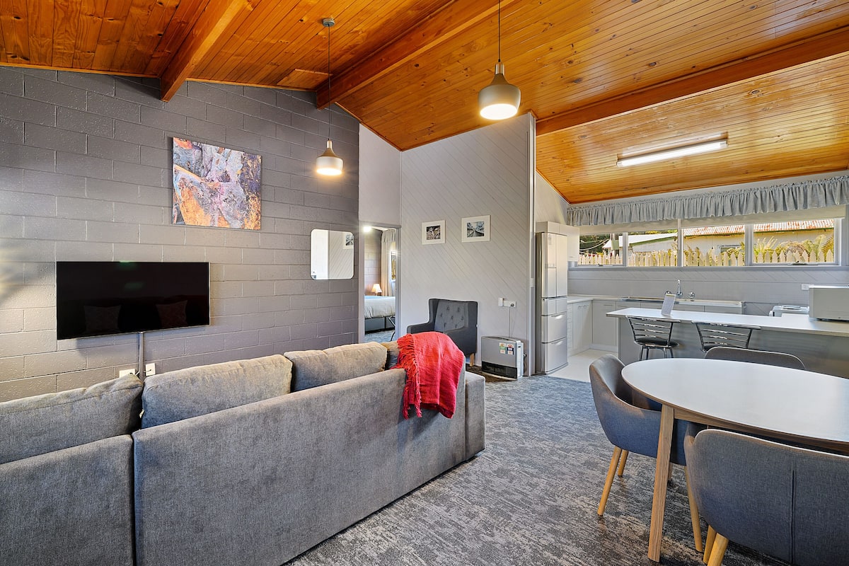 A modern living room with a grey sofa, a flat-screen TV, and a dining area with a round table and chairs.