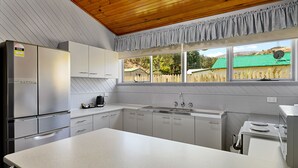 A modern kitchen with stainless steel appliances, white cabinetry, and a large window offering a view of a green-roofed house. - Gold Rush Inn (Queenstown)