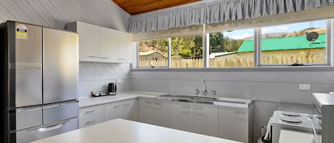 Una cocina moderna con electrodomésticos de acero inoxidable, armarios blancos y un ventanal con vistas a una casa con techo verde.