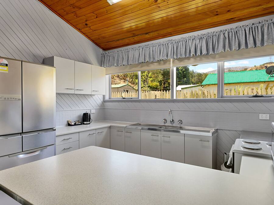 A modern kitchen with stainless steel appliances, white cabinetry, and a large window offering a view of a green-roofed house.