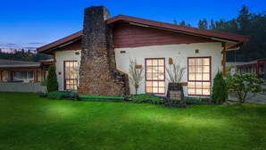 A two-story house with a stone chimney, a red roof, and a well-maintained lawn. - Gold Rush Inn (Queenstown)