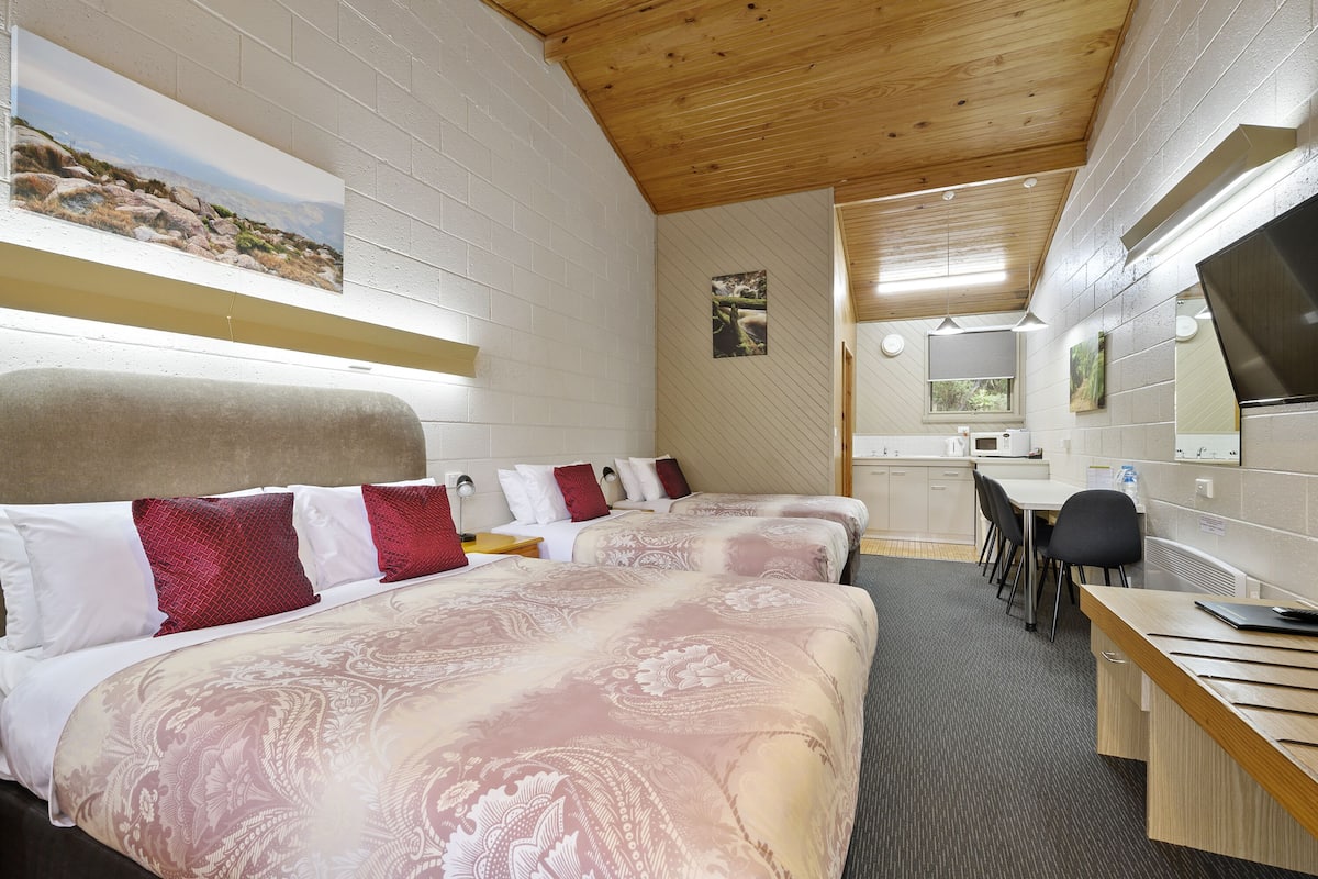 A hotel room with two beds, a desk, a chair, and a television.