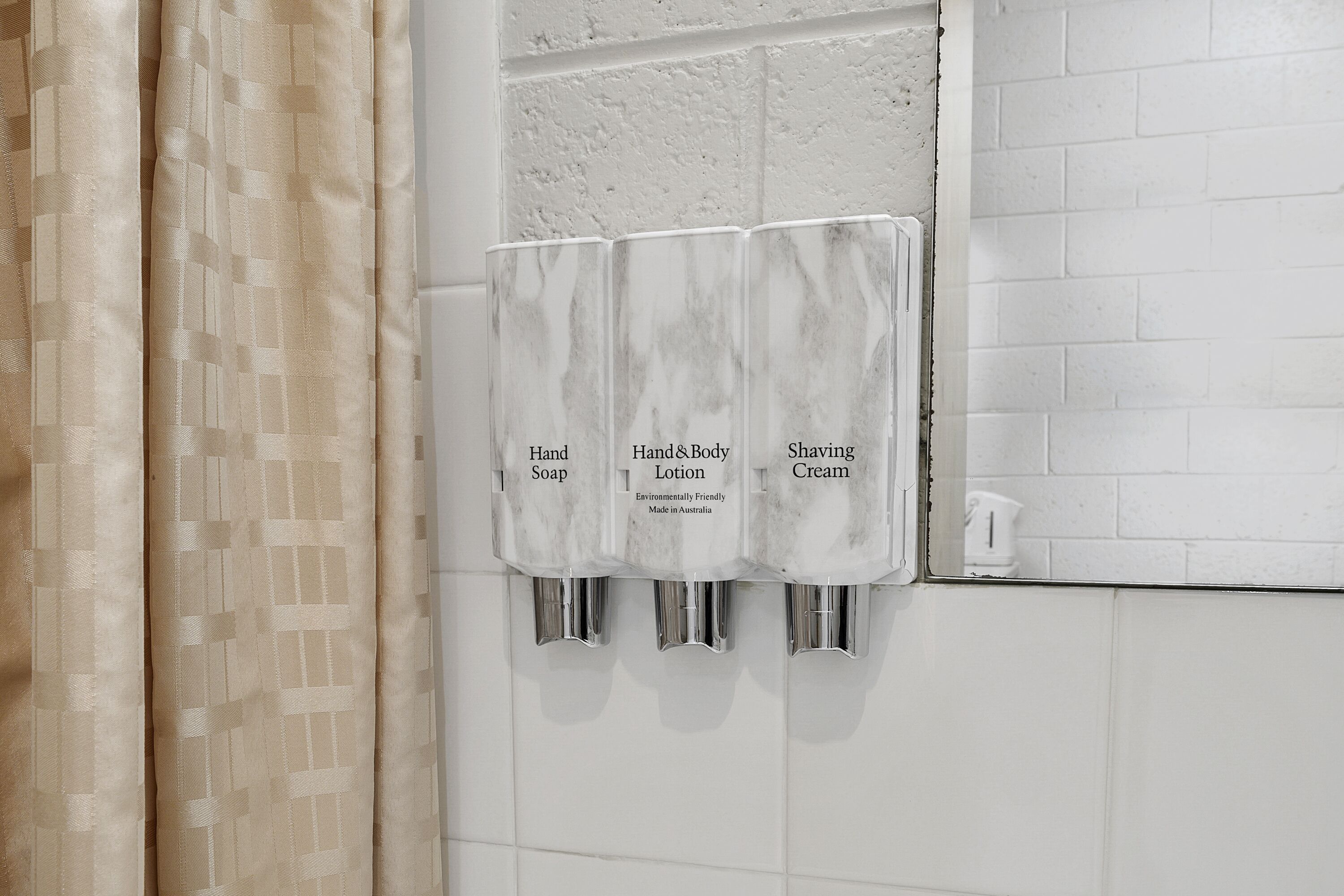 A bathroom with a marble soap dispenser wall, a white tiled wall, and a beige curtain.