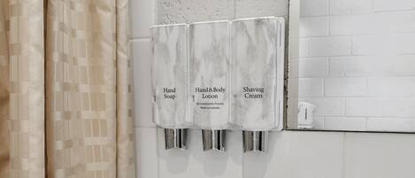 A bathroom with a marble soap dispenser wall, a white tiled wall, and a beige curtain.