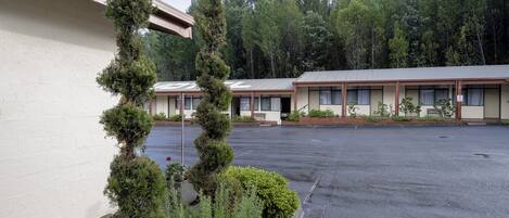 A motel with a parking lot, a row of rooms with awnings, and a forested backdrop.