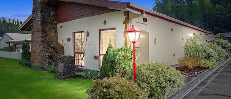 Uma casa com chaminé de pedra, um poste de rua vermelho e um gramado bem cuidado.