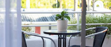 En balkon med et rundt bord, to fletstole og en potteplante.