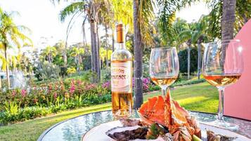 A table with a bottle of Provencal wine, two glasses of wine, a lobster, and oysters on a glass table outdoors.