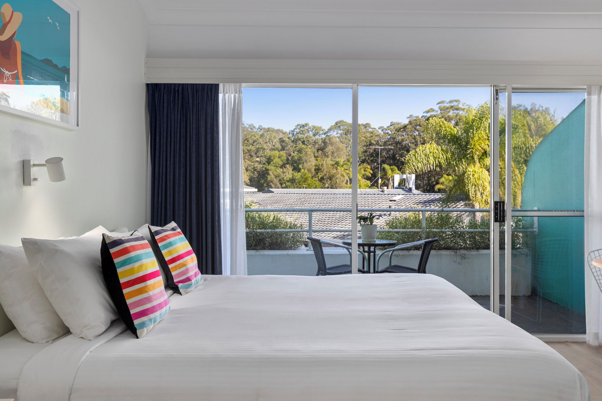 A bedroom with a large bed, a view of the outdoors, and a balcony with a table and chairs.