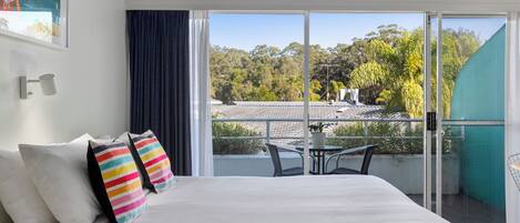 A bedroom with a large bed, a view of the outdoors, and a balcony with a table and chairs.