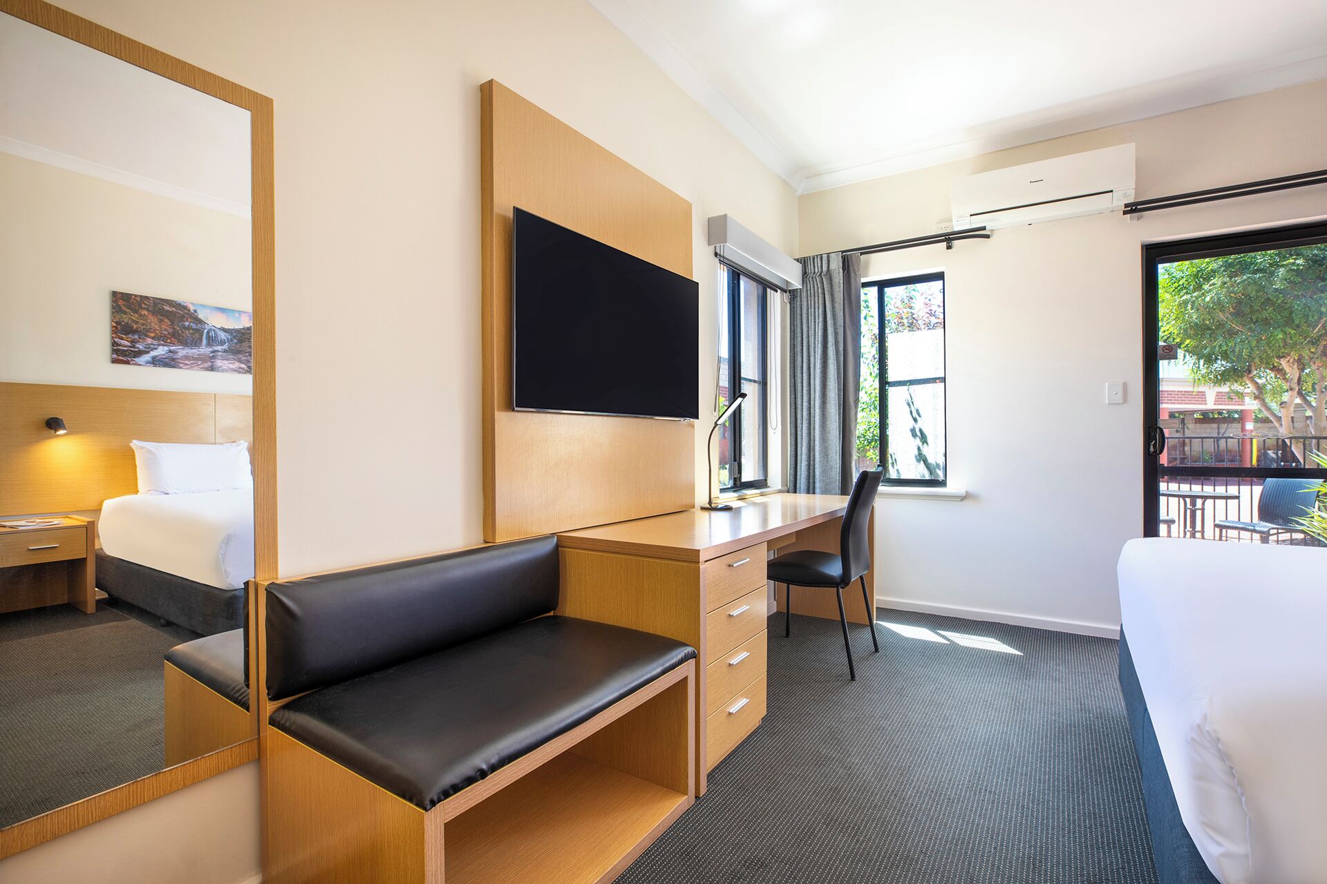 Habitación de hotel con cama, escritorio con silla, televisor montado en la pared y ventana con vistas al exterior.