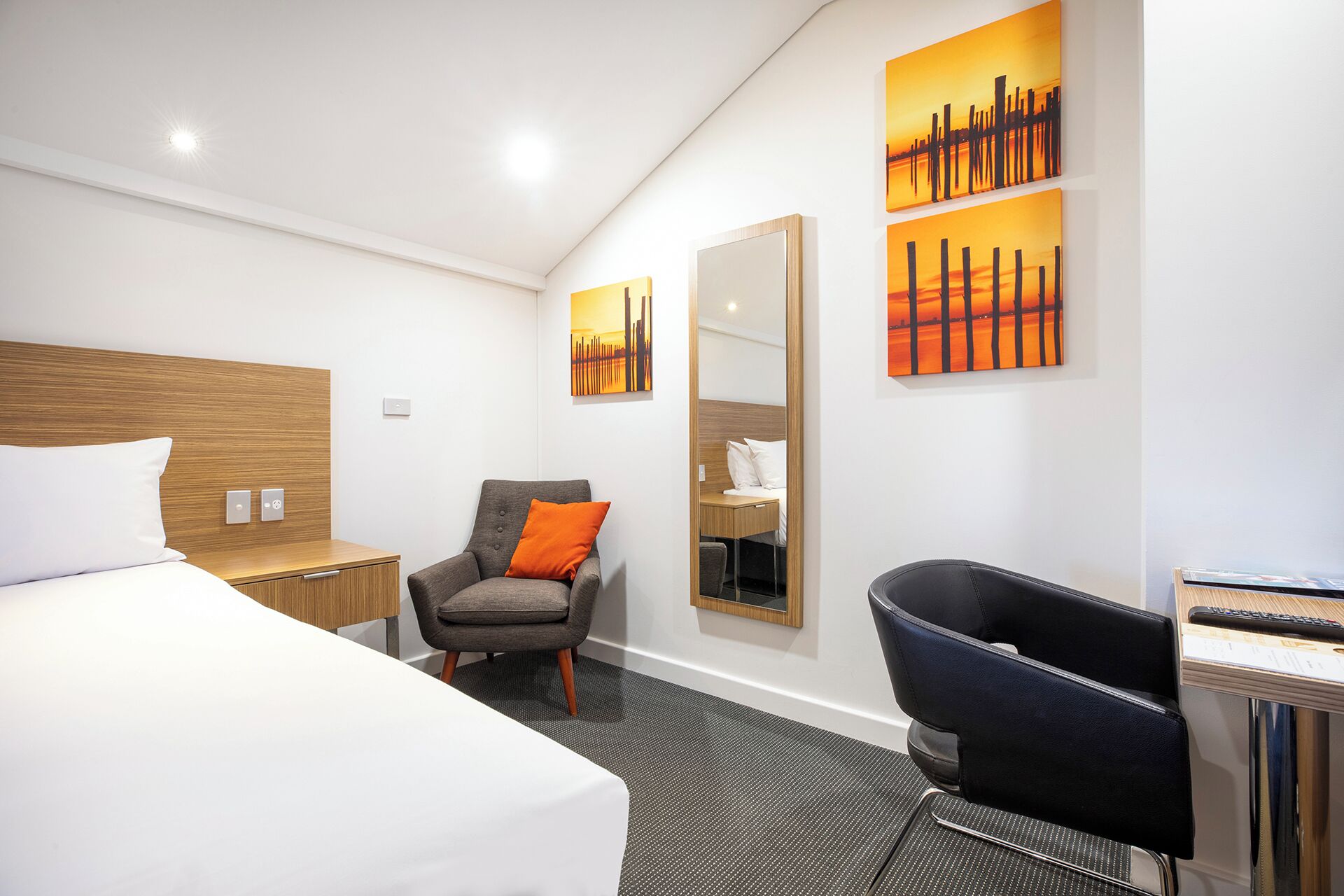 A modern hotel room with a large bed, a desk with a chair, a seating area with a chair and a sofa, and artwork on the walls.