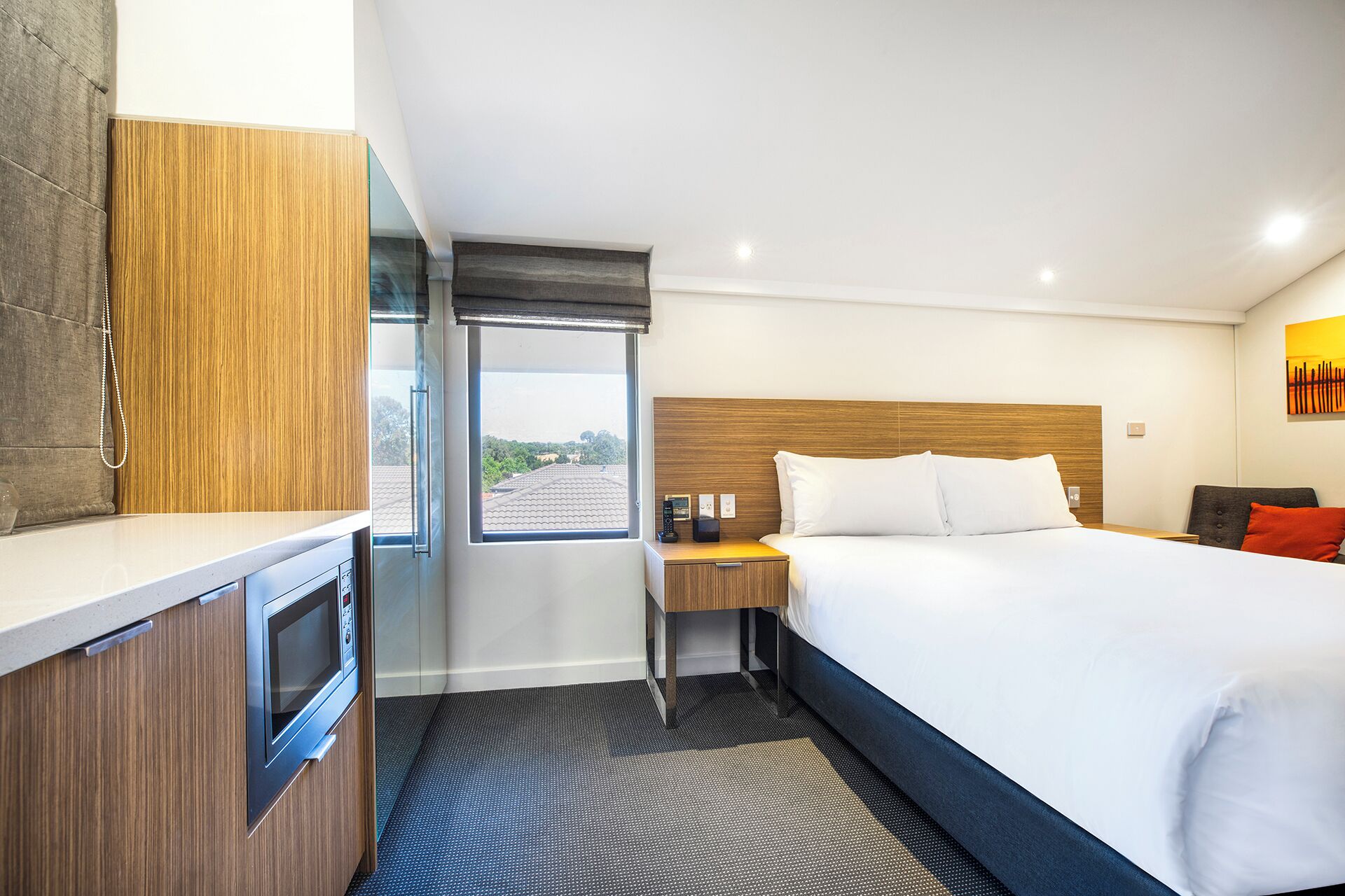 Habitación de hotel con cama, escritorio, microondas, ventana con vistas y cabecero de madera.