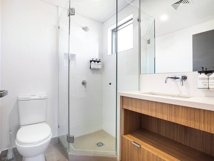 A modern bathroom with a glass-enclosed shower, a white toilet, and a vanity with a mirror and sink.