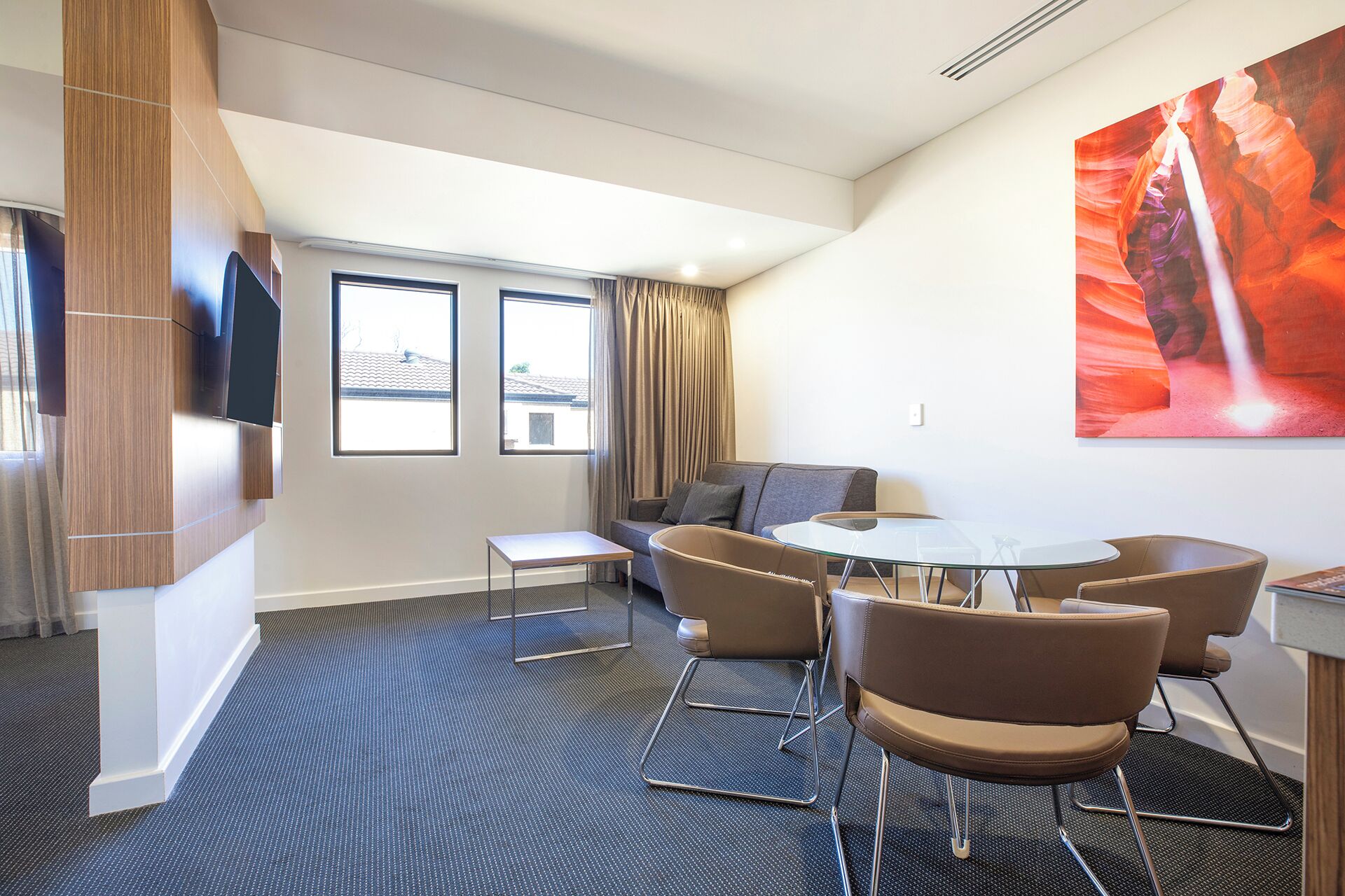 Una habitación de hotel moderna con un sofá, dos sillones, una mesita y un televisor fijado a un panel de madera.