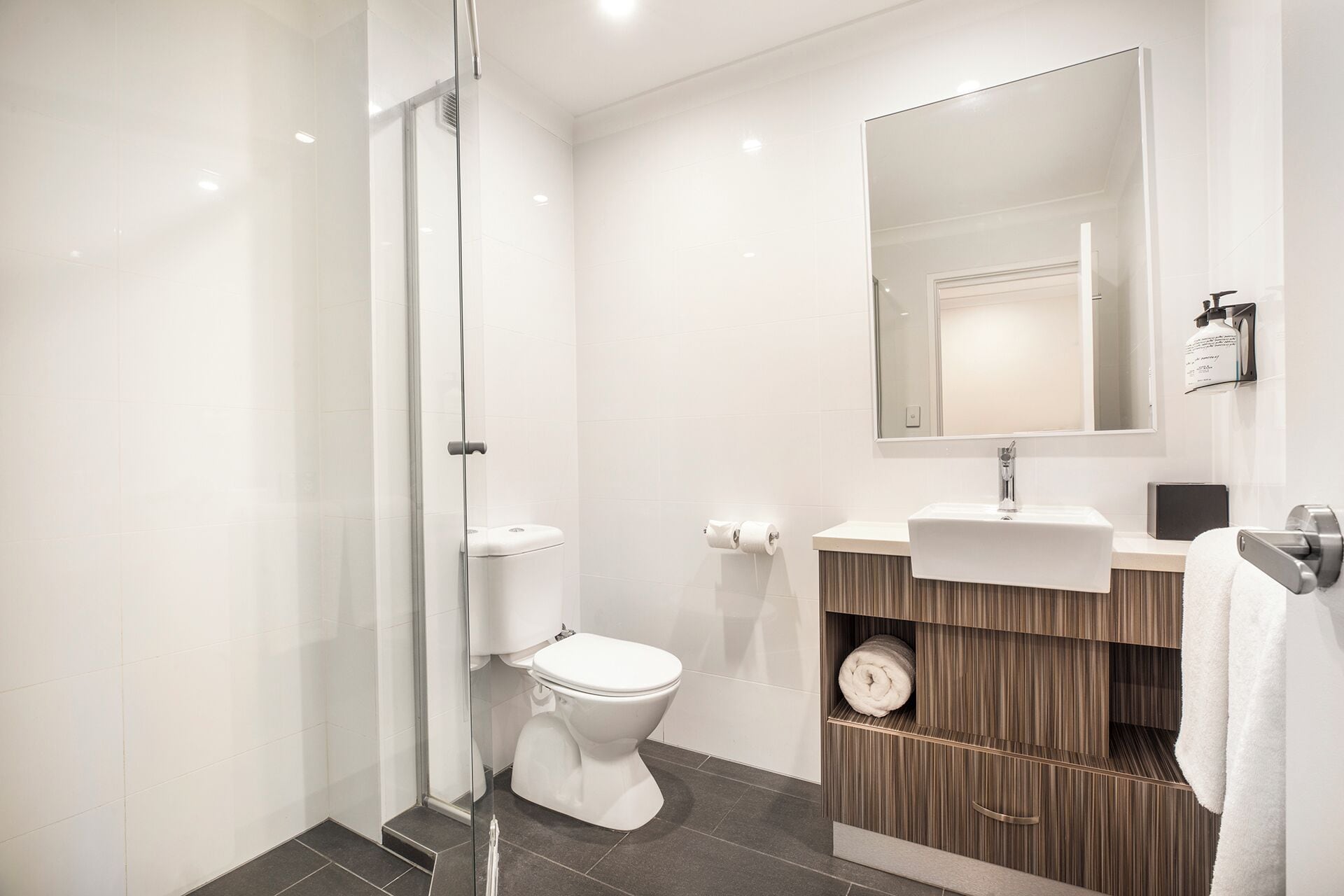 Un baño moderno con cabina de ducha de vidrio, inodoro, lavabo con espejo y perchero.
