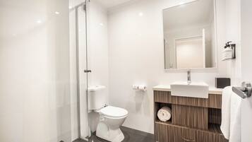 Un baño moderno con cabina de ducha de vidrio, inodoro, lavabo con espejo y perchero.