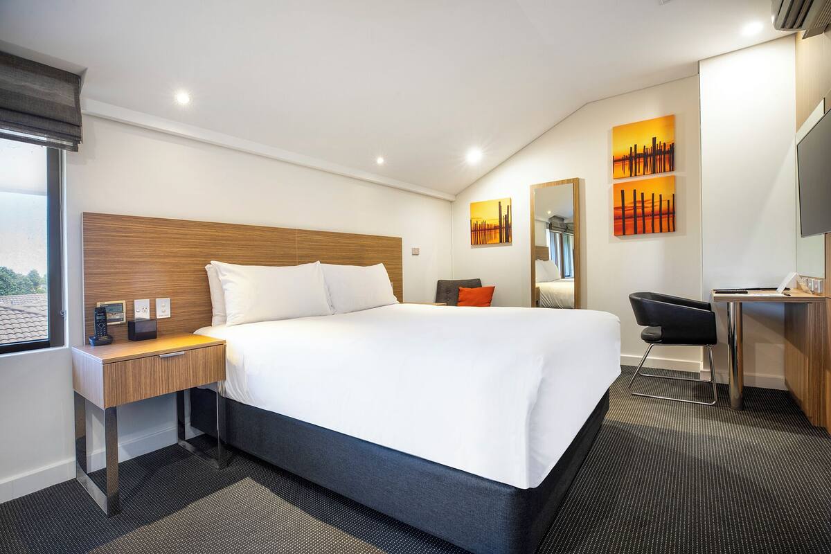 Una habitación de hotel moderna con una cama grande, un escritorio, una silla y una lámpara de escritorio.