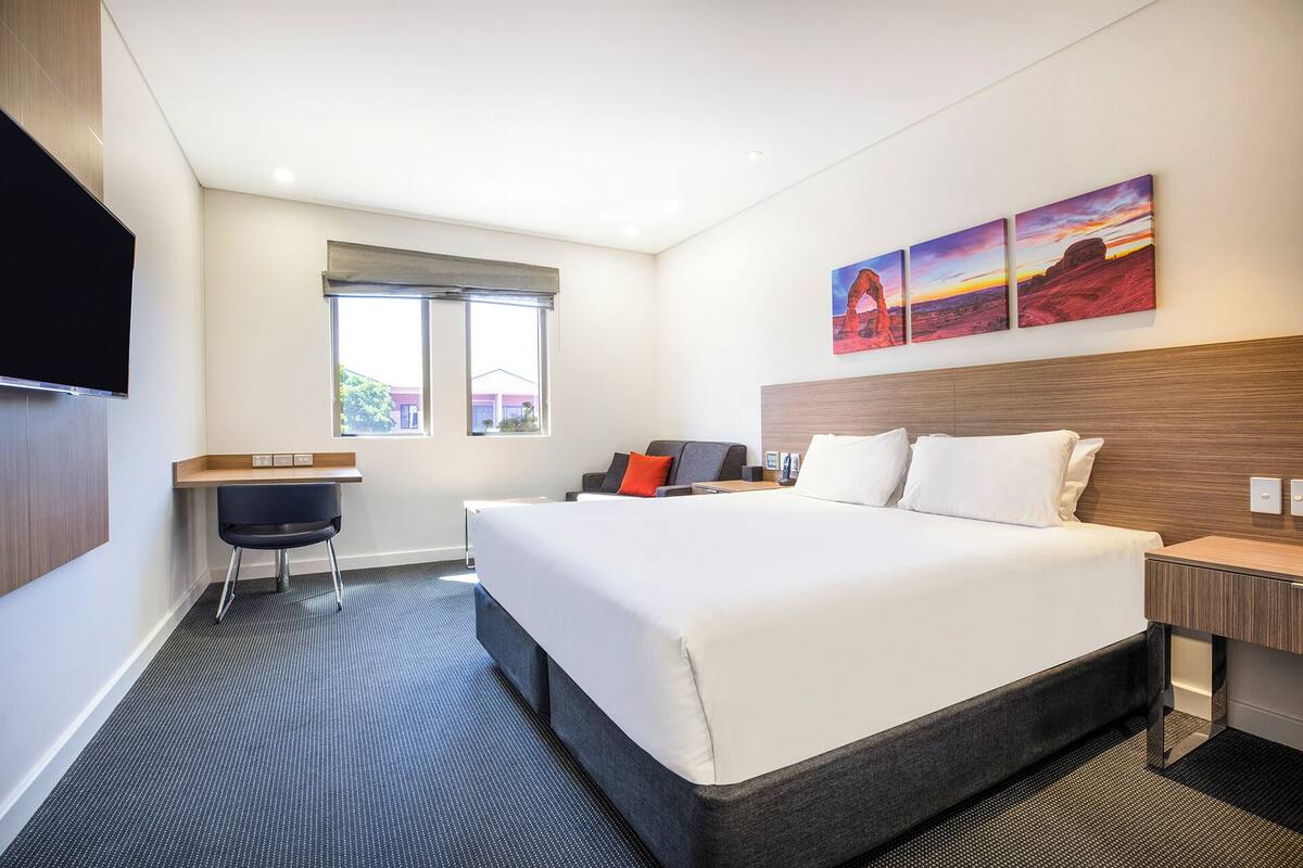 Una habitación de hotel con una cama grande, un escritorio, una silla y un televisor.