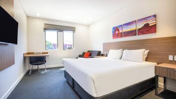 A hotel room with a large bed, a desk, a chair, and a TV.