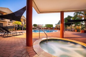 Un espace piscine comprenant des chaises longues, un jacuzzi et un coin salon abrité.