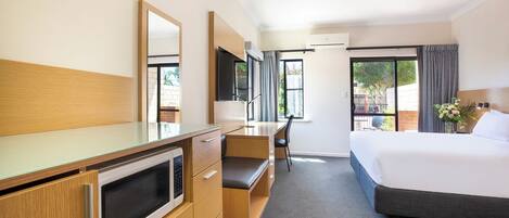 Una habitación de hotel con una cama, un escritorio con una silla, un televisor y un ventanal amplio.