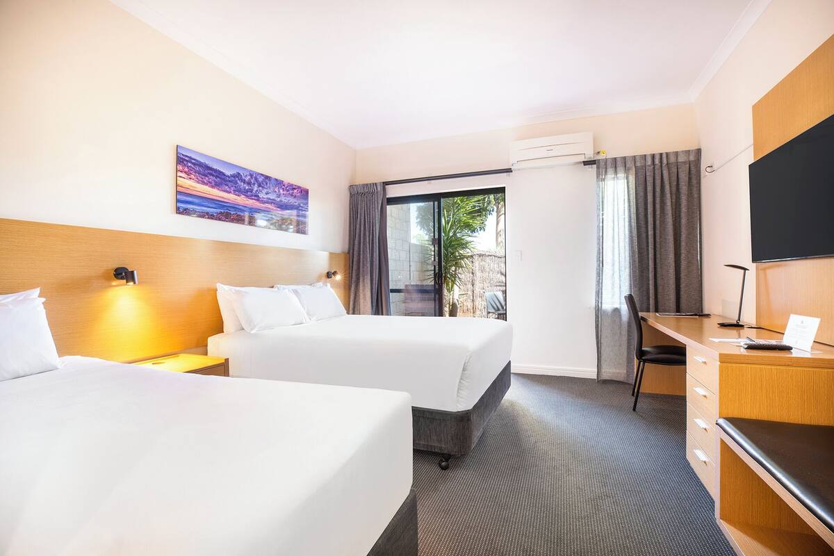 Habitación de hotel con dos camas, un escritorio con una silla, un televisor y un cuadro en la pared.