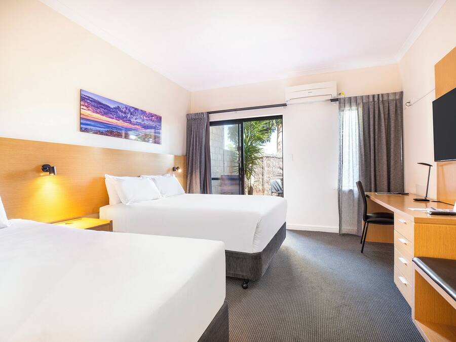 A hotel room with two beds, a desk with a chair, a TV, and a painting on the wall.