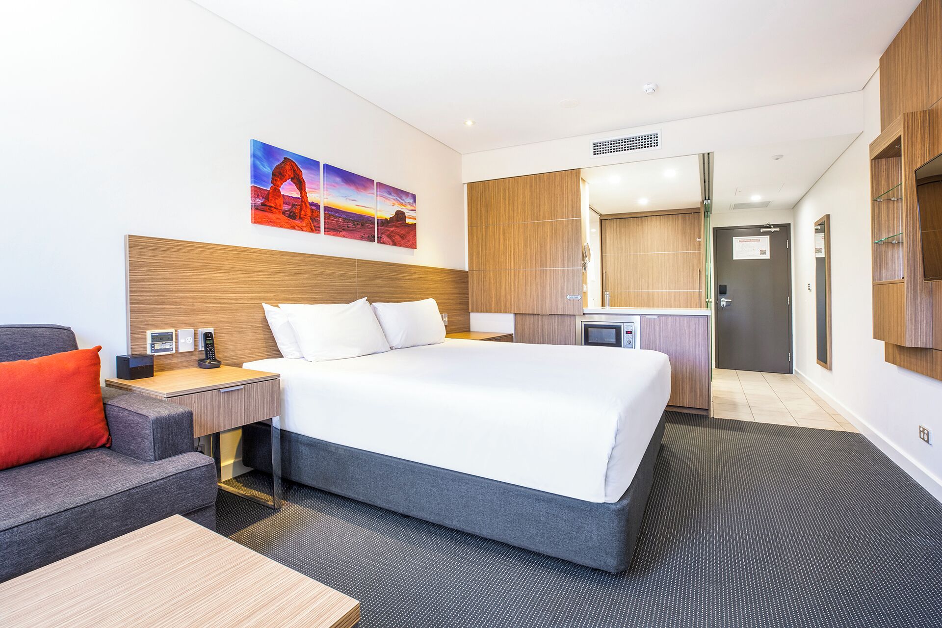 Una habitación de hotel moderna con una cama grande, un escritorio con computadora, un sofá y un cuadro de un paisaje.
