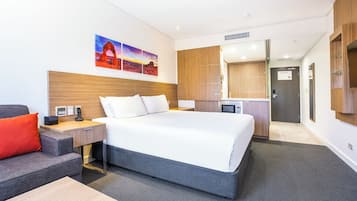 Una habitación de hotel moderna con una cama grande, un escritorio con computadora, un sofá y un cuadro de un paisaje.