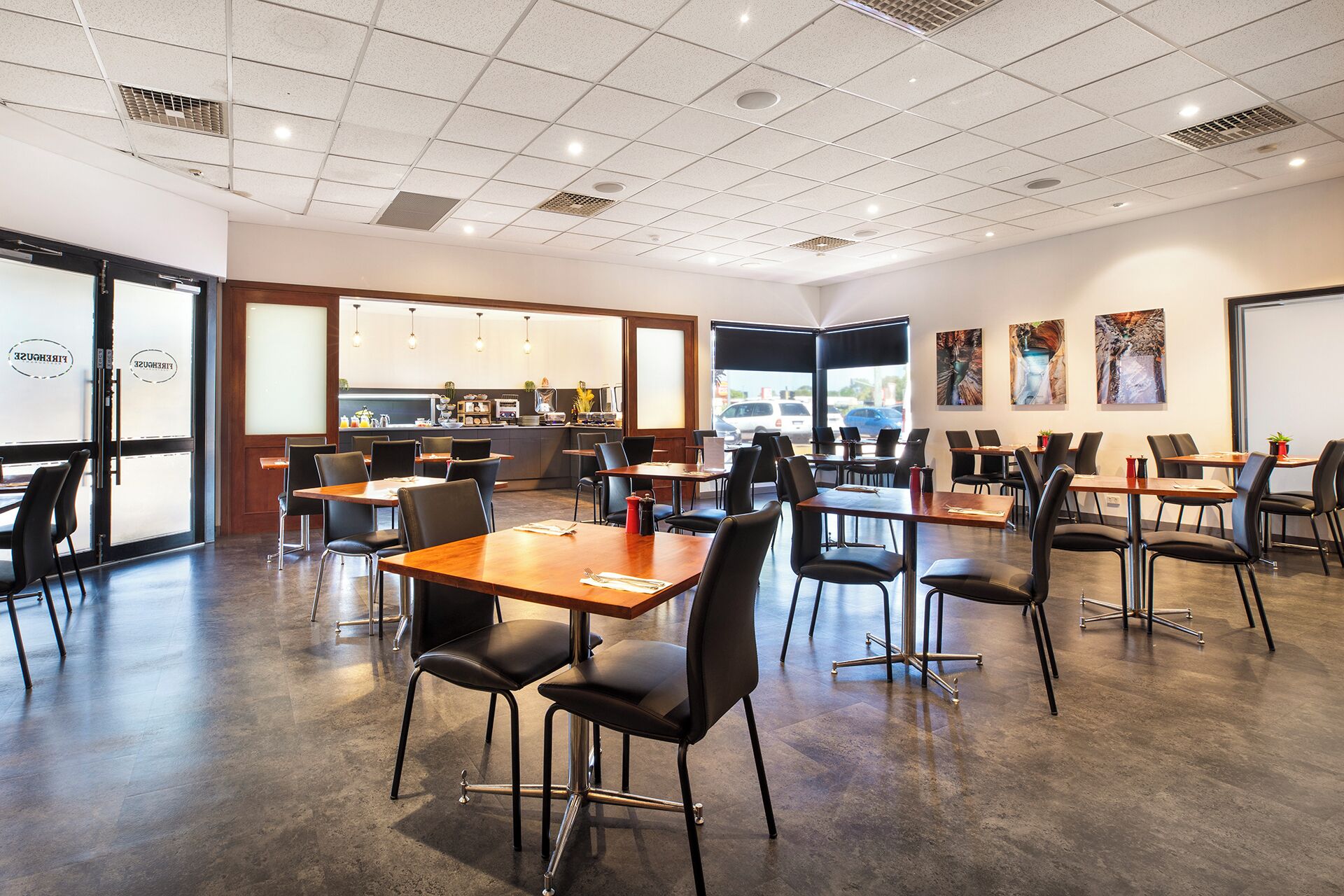 Um restaurante moderno com disposição ampla e arejada, cadeiras pretas e mesas de madeira.