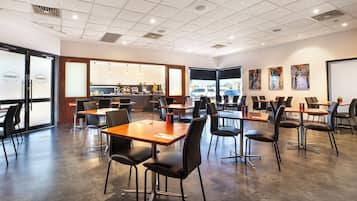 Um restaurante moderno com disposição ampla e arejada, cadeiras pretas e mesas de madeira.