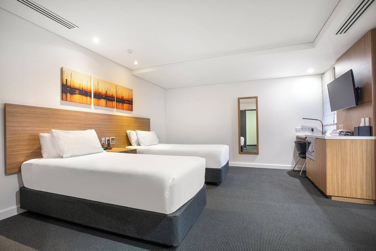Habitación de hotel con dos camas, un escritorio, un televisor de pantalla plana y un cuadro en la pared.