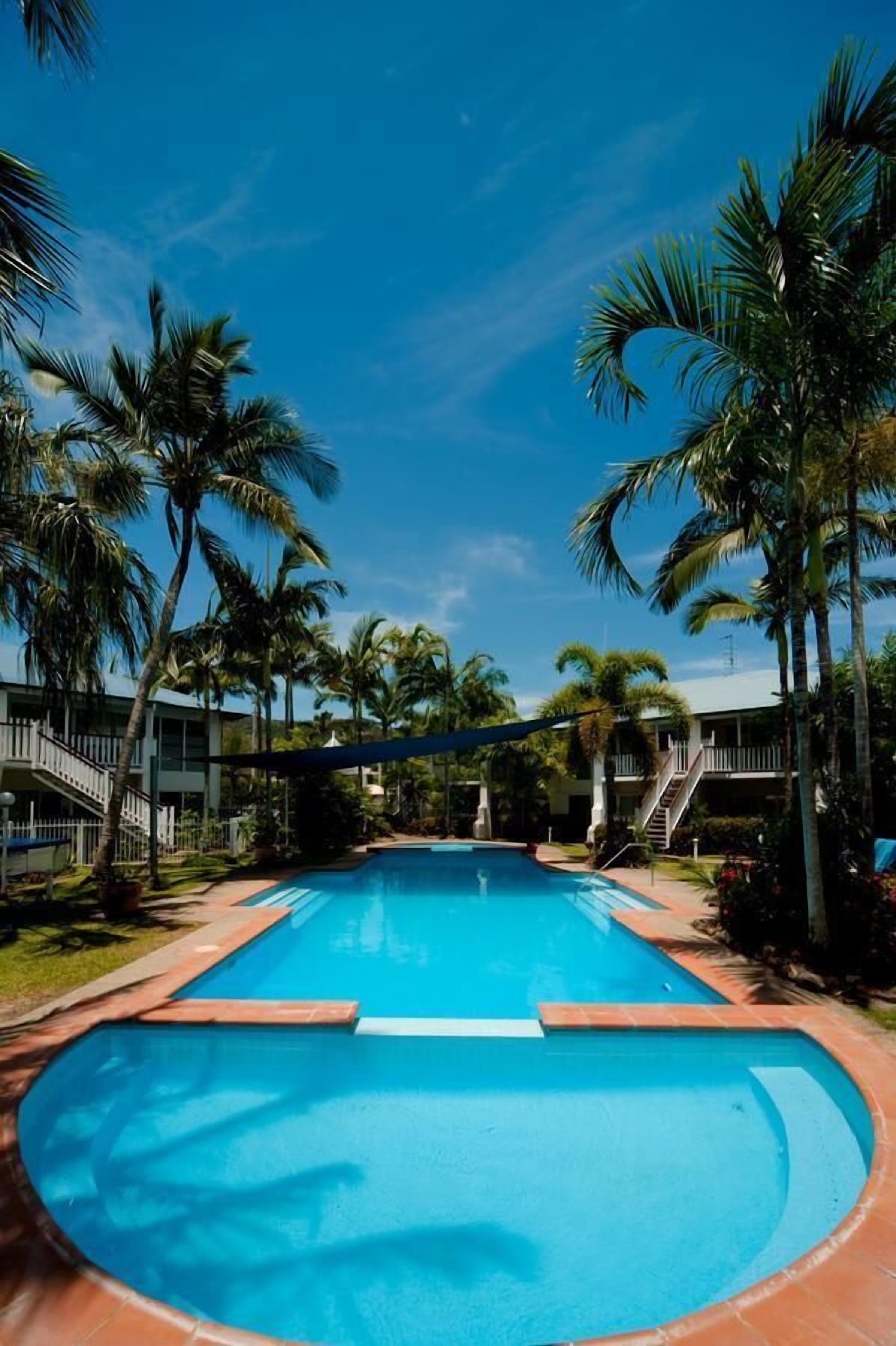 Piscina cercada por palmeiras e um edifício com escadaria.