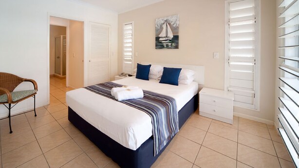 A bedroom with a bed, a chair, a bedside table, a painting, and a window with blinds. - Mango House Resort (Jubilee Pocket)