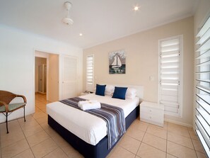 A bedroom with a bed, a chair, a bedside table, a painting, and a window with blinds. - Mango House Resort (Jubilee Pocket)