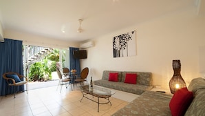 A living room with a sofa, chairs, a coffee table, and a TV. There is a staircase leading to a balcony with plants. - Mango House Resort (Jubilee Pocket)