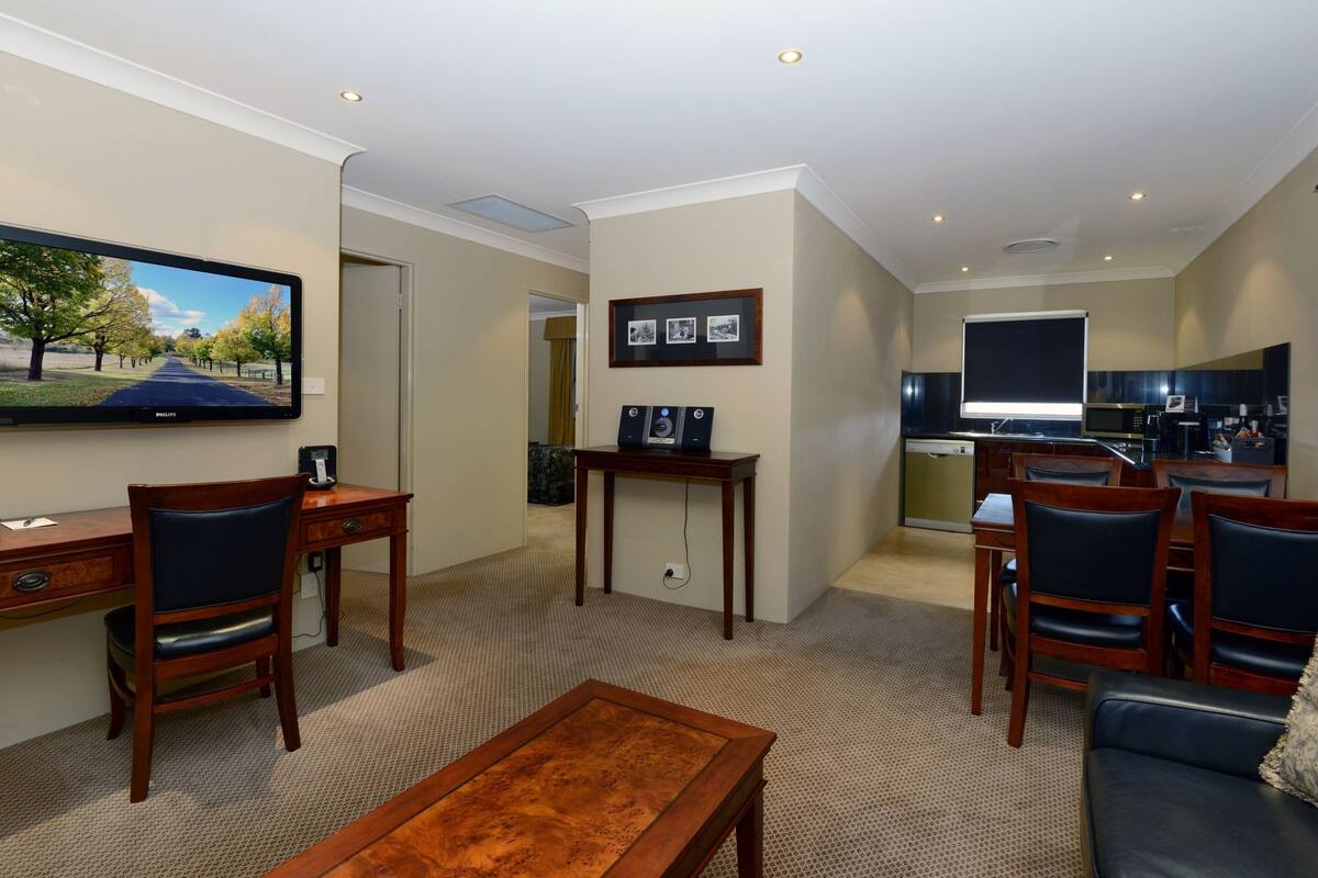 A modern living room with a flat-screen TV, wooden furniture, a dining area, and a kitchen.