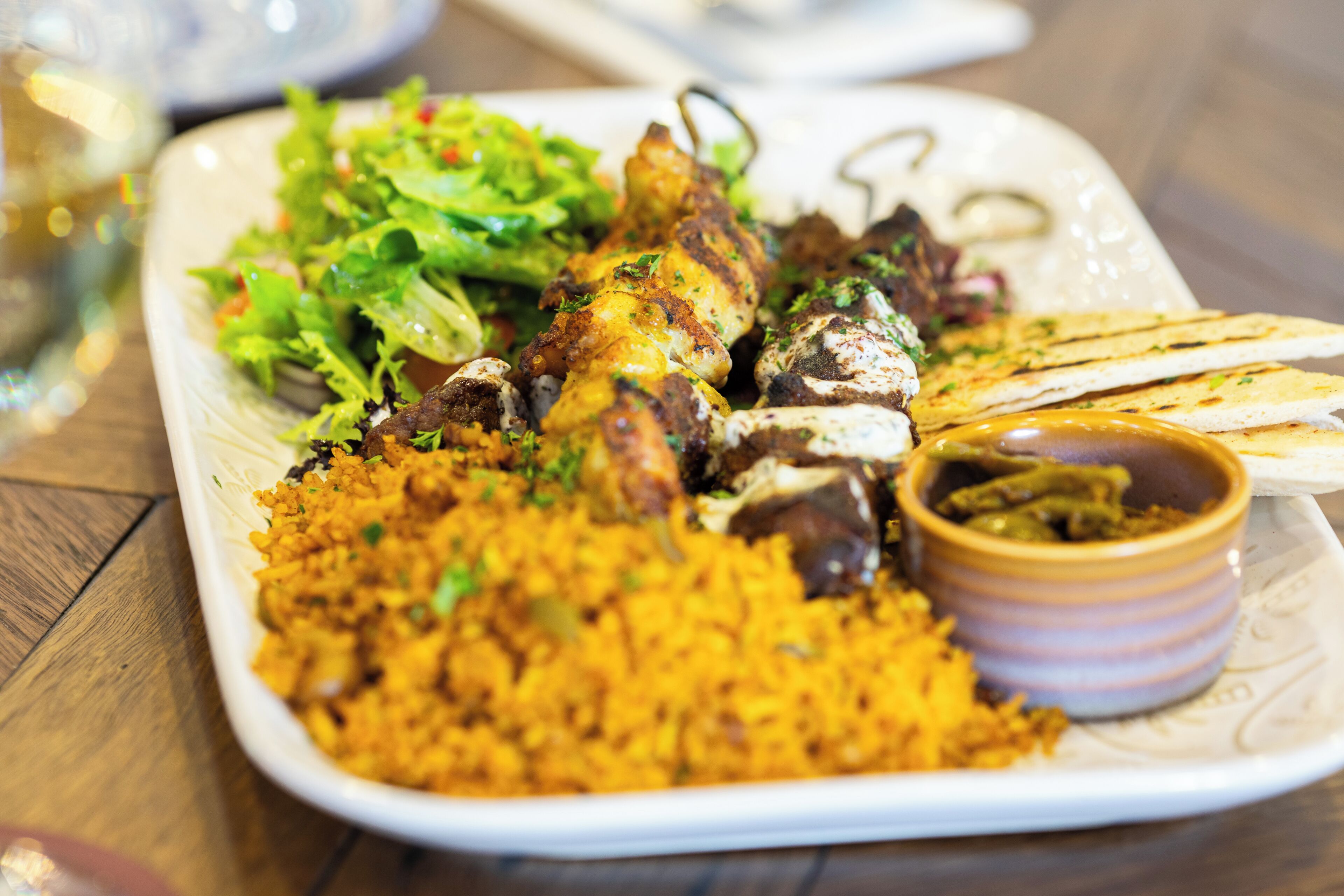 A plate with grilled chicken, rice, salad, and flatbread.