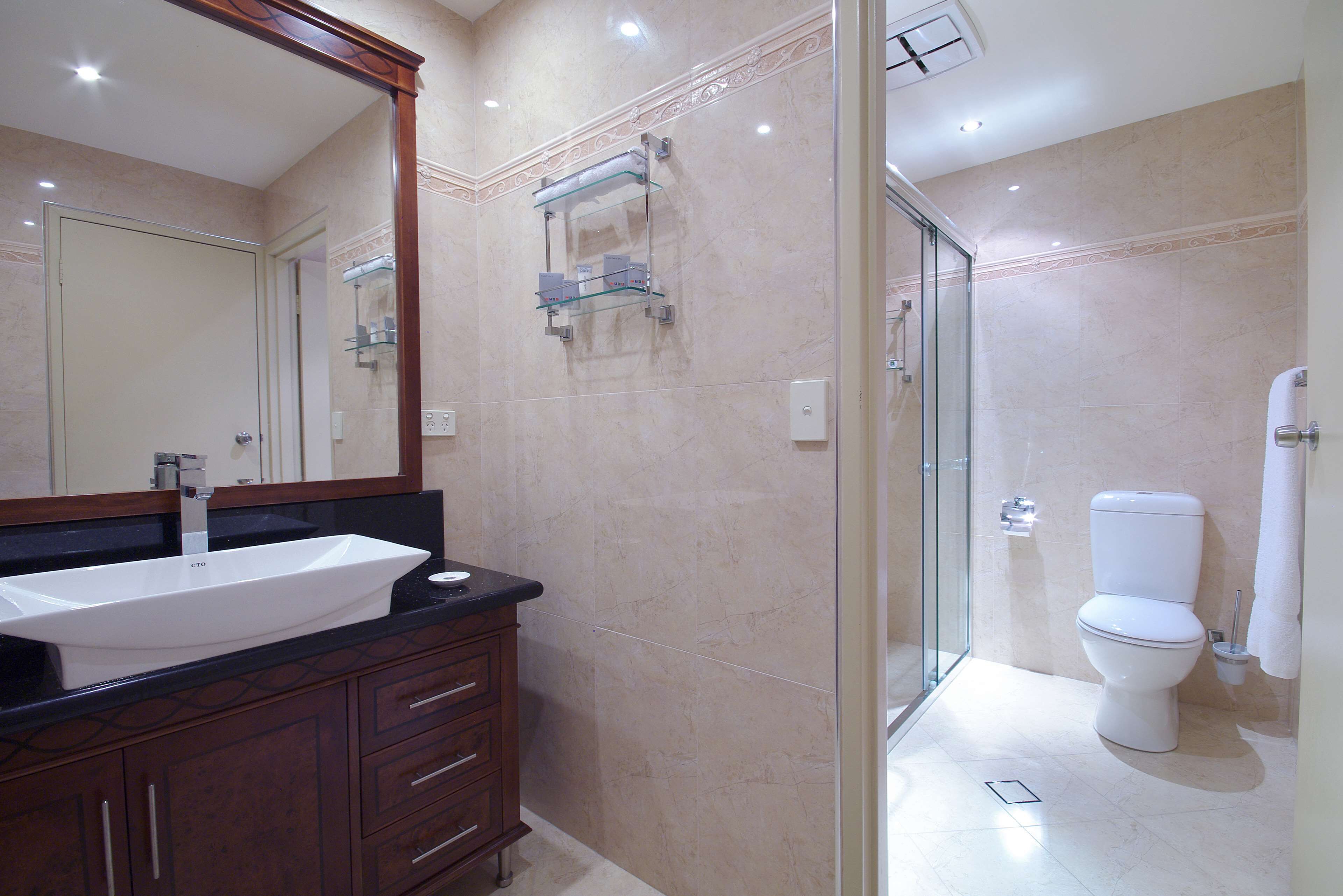 A bathroom with a large mirror, a sink, a toilet, and a shower area.