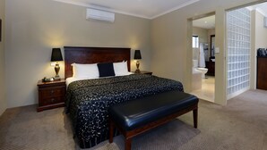 A hotel bedroom with a large bed, bedside lamps, a bench, and a view of the bathroom through an open door. - Rydges Armidale (Armidale)