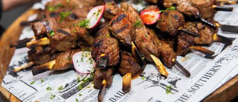Skewered meat on a wooden board with newspaper underneath.