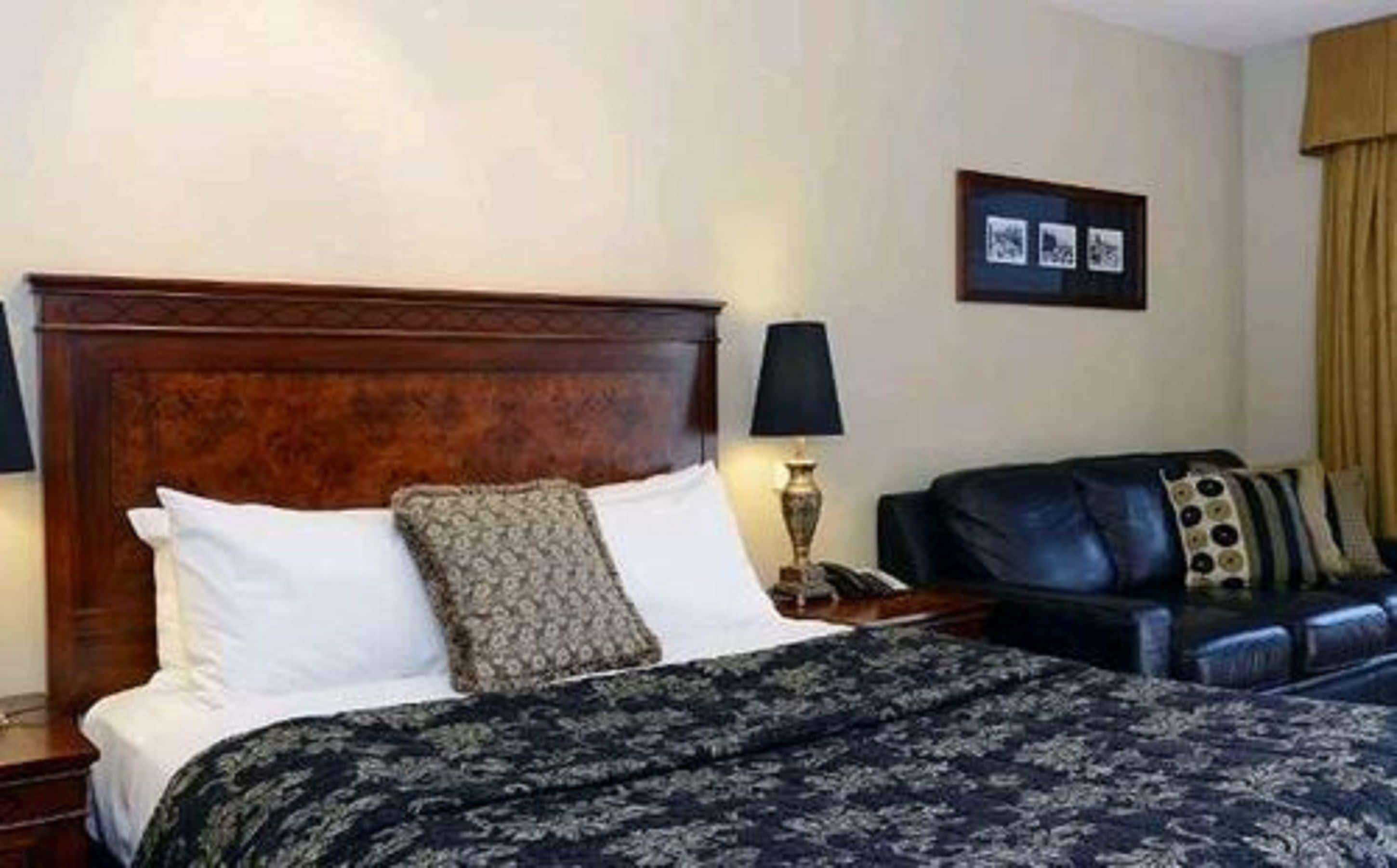 A hotel room with a large bed, a bedside table, a lamp, a black leather sofa, and a framed picture on the wall.